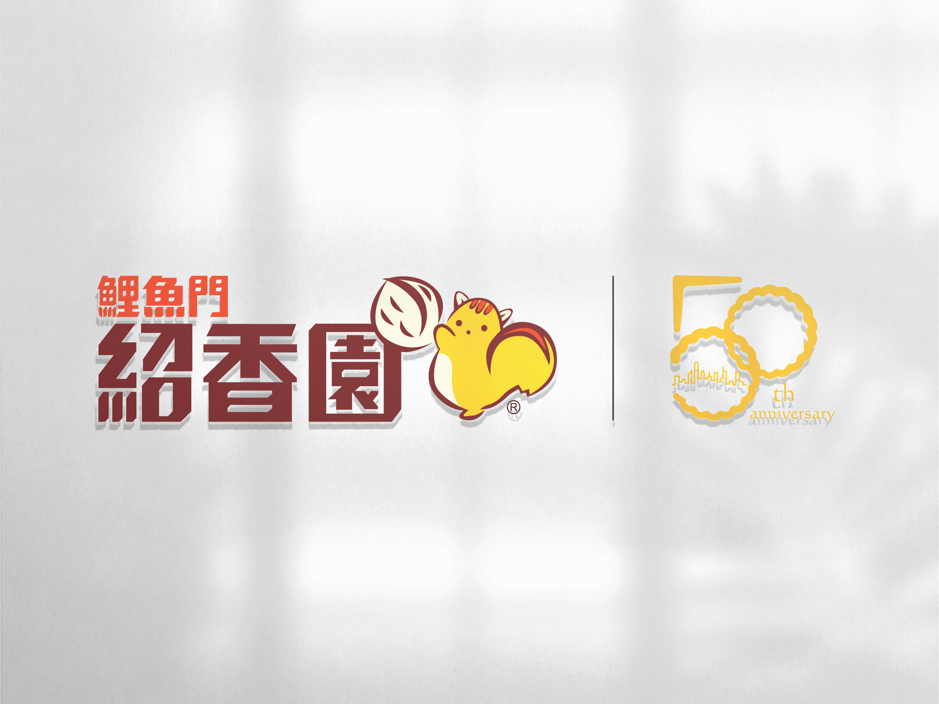 A logo featuring a red and brown text with a yellow squirrel mascot holding a nut, alongside a 50th-anniversary emblem in gold. The background is slightly blurred.